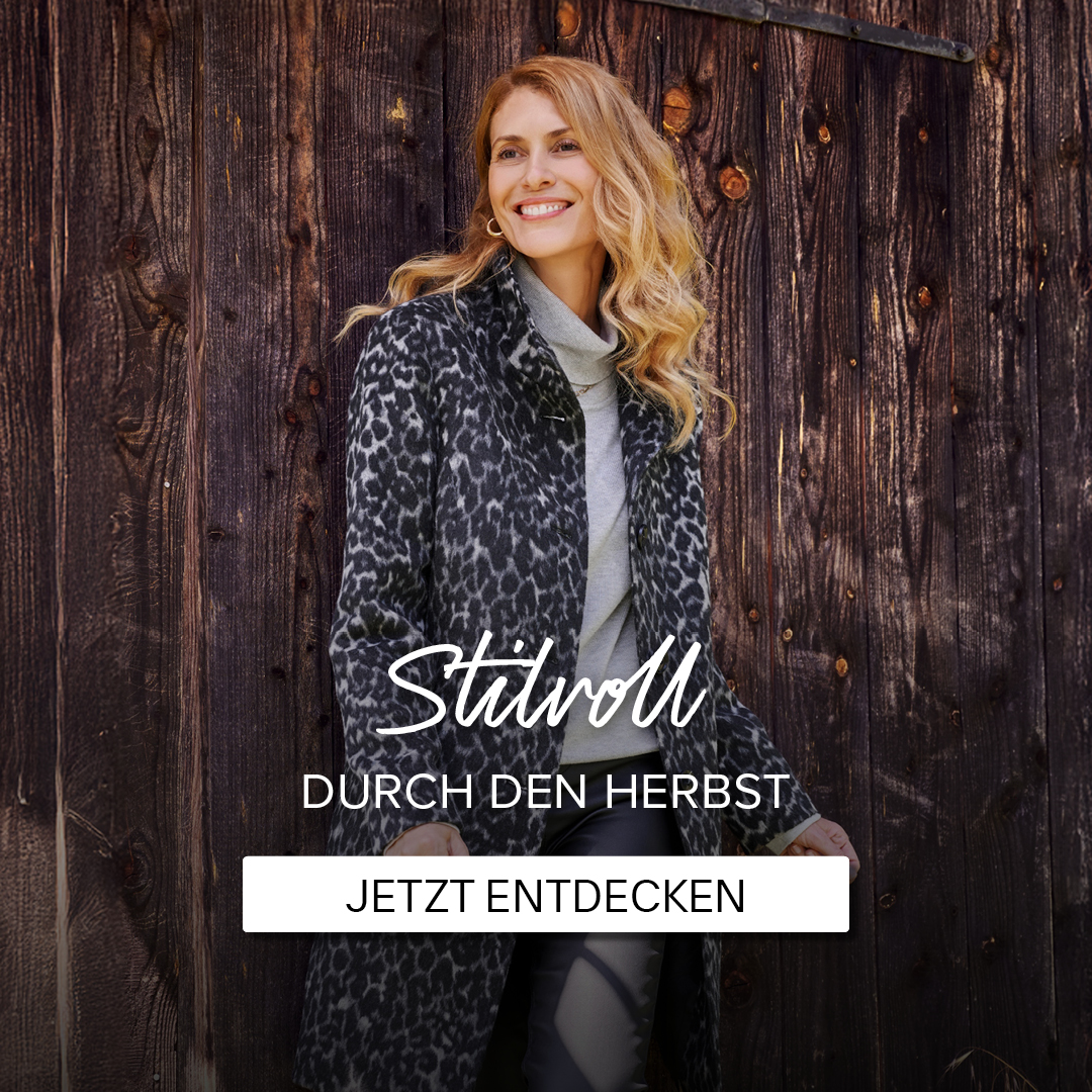 Eine Frau in einem modischen, leopardgemusterten Mantel steht an einer Holzwand. Text: "Stilvoll durch den Herbst - Jetzt entdecken."
