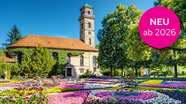 Eine Kirche umgeben von bunten Blumenbeeten und Bäumen.
