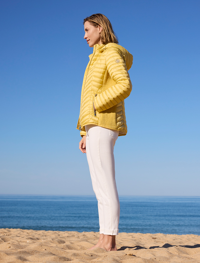 Eine Frau in einer gelben Jacke steht am Strand und genießt die Aussicht auf das Meer.