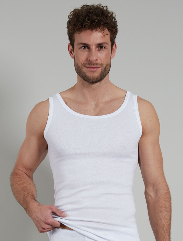 Ein Mann in einem weißen Tanktop und Unterwäsche posiert vor neutralem Hintergrund. Ein Mann in einem weißen Tanktop und Unterwäsche posiert vor neutralem Hintergrund.