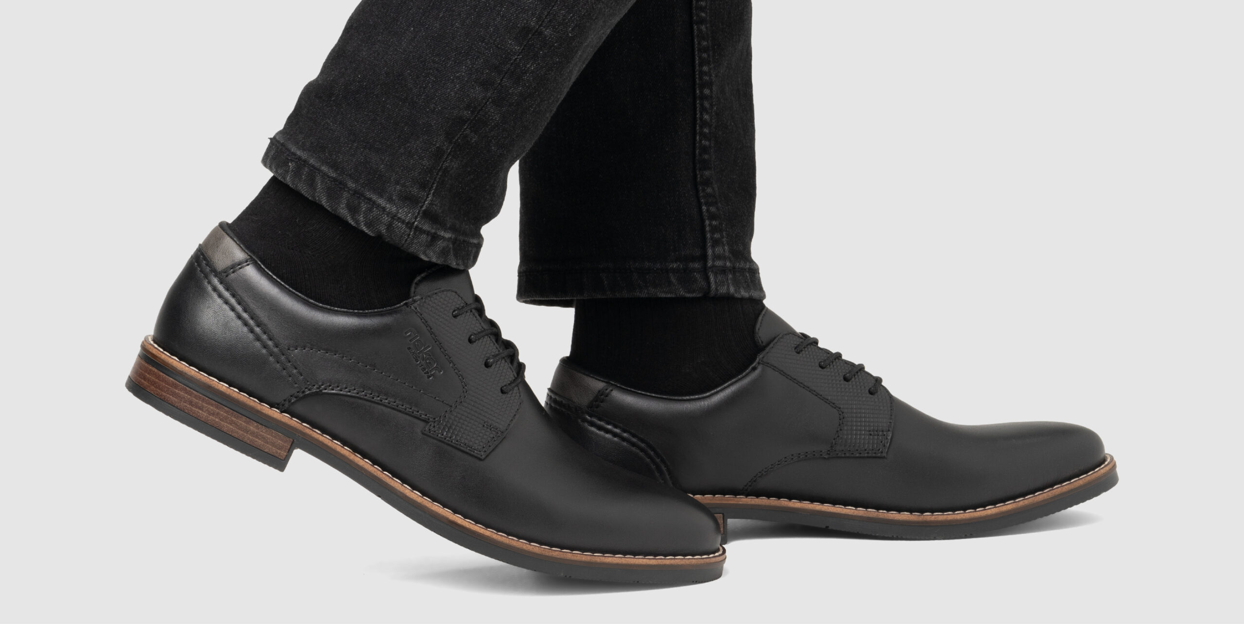 Schwarze Herrenschuhe aus Leder mit brauner Sohle, getragen zu schwarzen Socken und dunkler Hose Schwarze Herrenschuhe aus Leder mit brauner Sohle, getragen zu schwarzen Socken und dunkler Hose