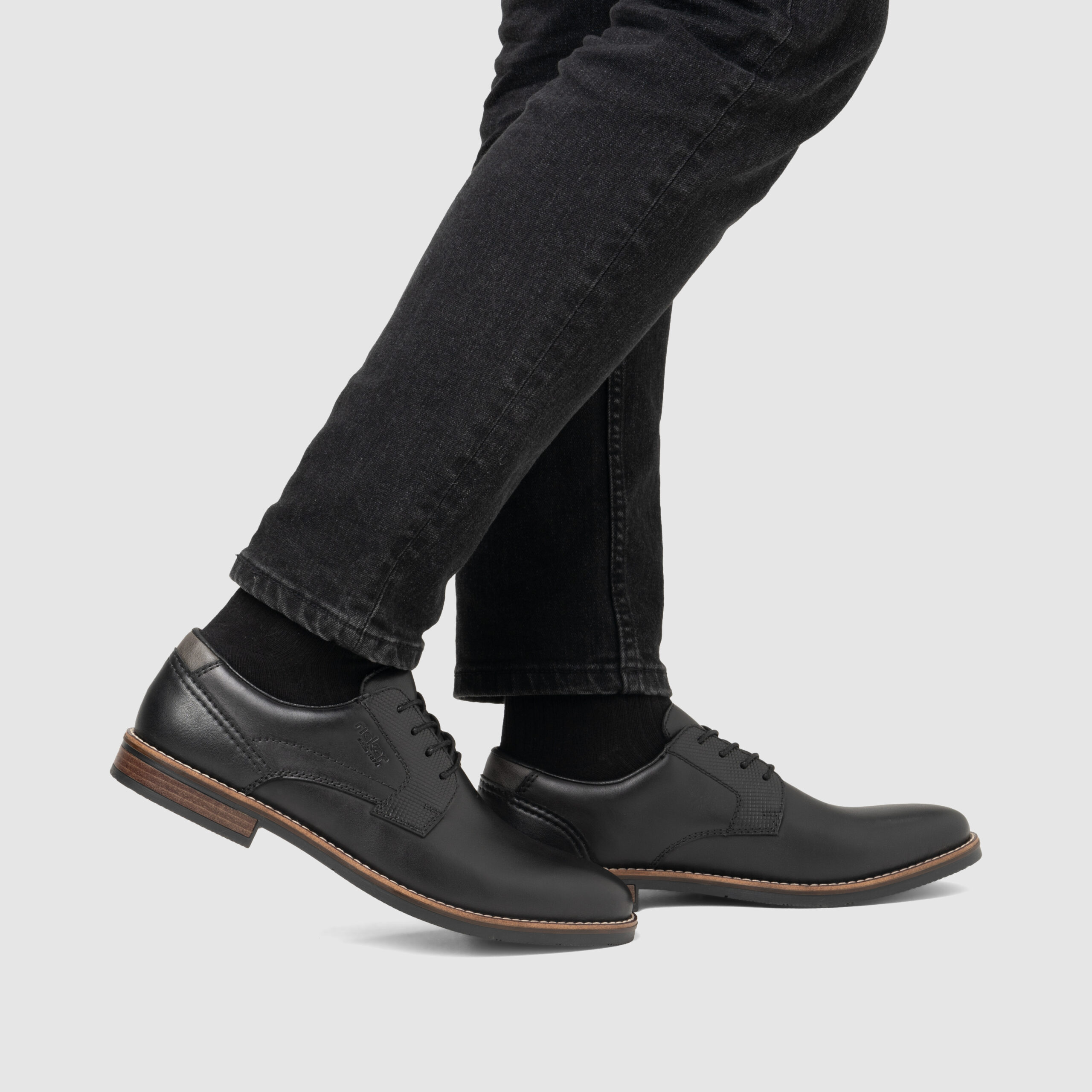 Schwarze Herrenschuhe aus Leder mit brauner Sohle, getragen zu schwarzen Socken und dunkler Hose Schwarze Herrenschuhe aus Leder mit brauner Sohle, getragen zu schwarzen Socken und dunkler Hose