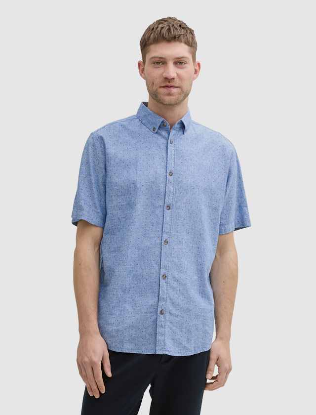 Ein Mann steht in einem blauen, kurzärmeligen Hemd mit Muster. Ein Mann steht in einem blauen, kurzärmeligen Hemd mit Muster.