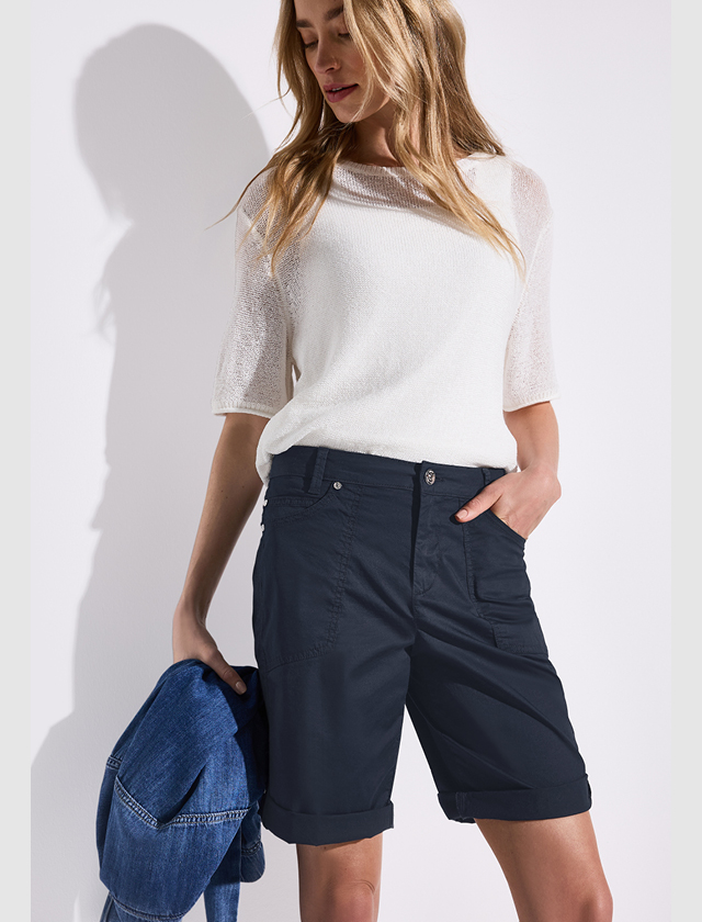 Eine Frau trägt ein helles Oberteil und dunkelblaue Shorts, während sie eine Jeansjacke in der Hand hält. Eine Frau trägt ein helles Oberteil und dunkelblaue Shorts, während sie eine Jeansjacke in der Hand hält.