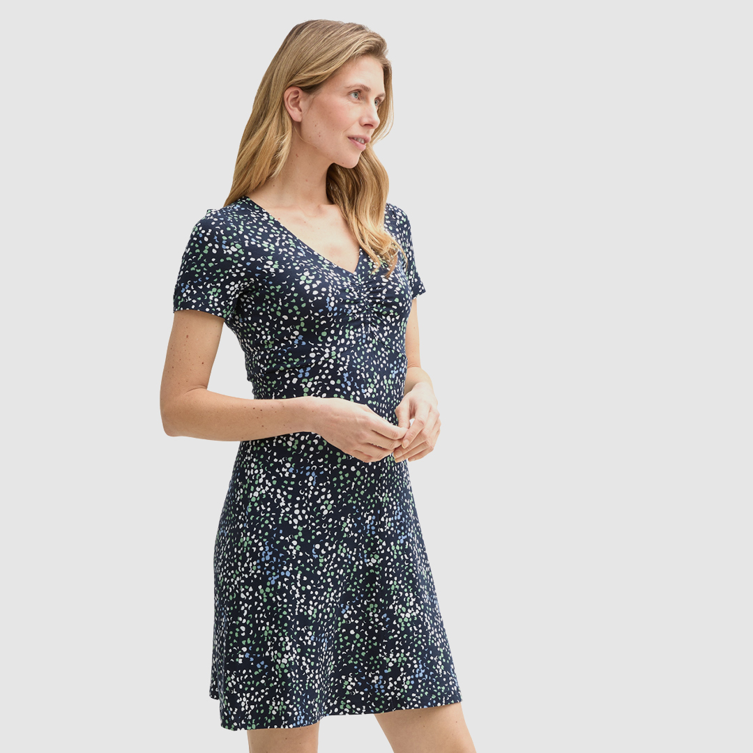 Eine Frau trägt ein Kleid mit kurzem Arm in dunklem Blau mit bunten Punkten.