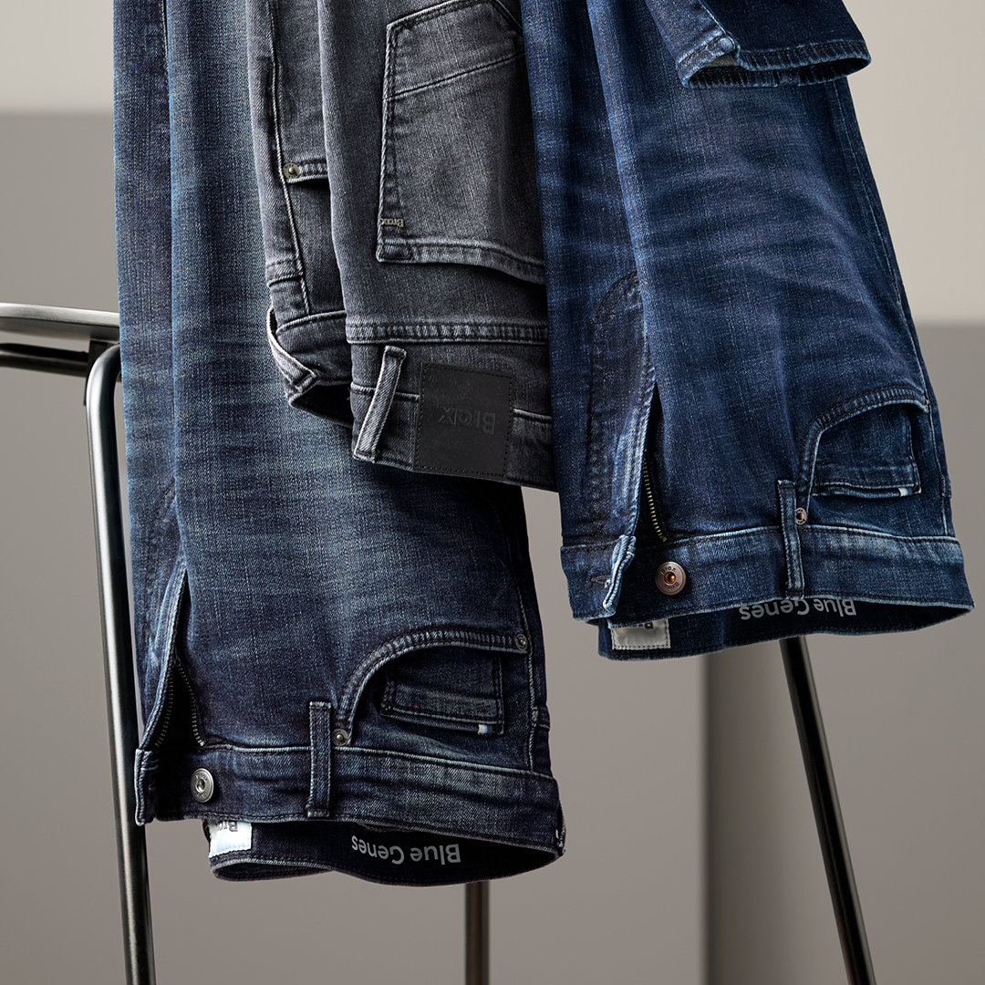 Mehrere dunkelblaue Jeanshosen hängen über einer schwarzen Metallstange, sichtbar sind Taschen, Nähte und Knöpfe.