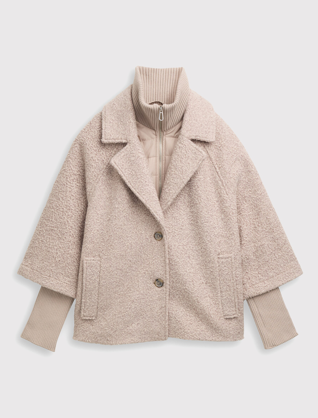 Beige, kurz geschnittener Mantel mit zwei Knöpfen, breitem Reverskragen und seitlichen Taschen über einem beigen, hochgeschlossenen Pullover mit Reißverschluss. Beige, kurz geschnittener Mantel mit zwei Knöpfen, breitem Reverskragen und seitlichen Taschen über einem beigen, hochgeschlossenen Pullover mit Reißverschluss.